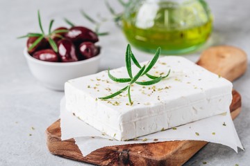 Homemade greek cheese feta with rosemary and herbs on cutting board with olive oil and olives - obrazy, fototapety, plakaty