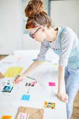 Teenage student standing by desk and looking through pictures while selecting some for her school project