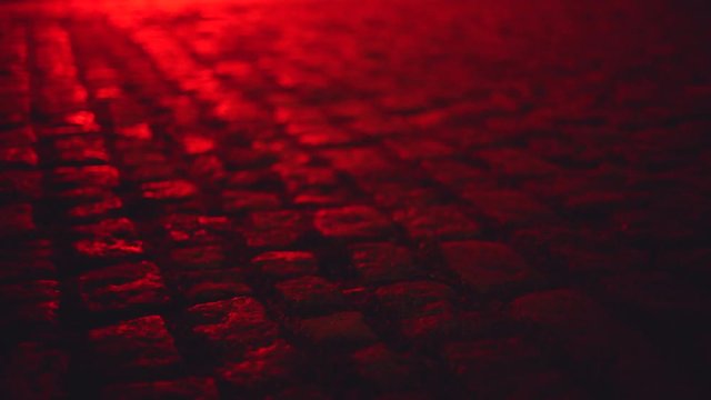 Wet illuminated by red light cobblestone paving street at night