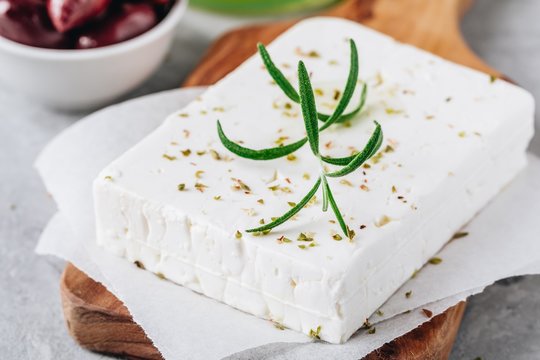 Homemade greek cheese feta with rosemary and herbs on cutting board with olive oil and olives