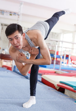 Positive man  acrobat exercising gymnastic action at sport gym