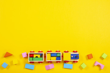 Wooden kid baby toys background. Eco friendly toy train and colorful blocks on yellow background