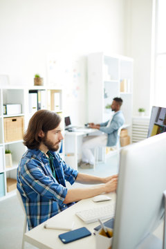 Serious young software developer sitting in front of one of monitors and coding data