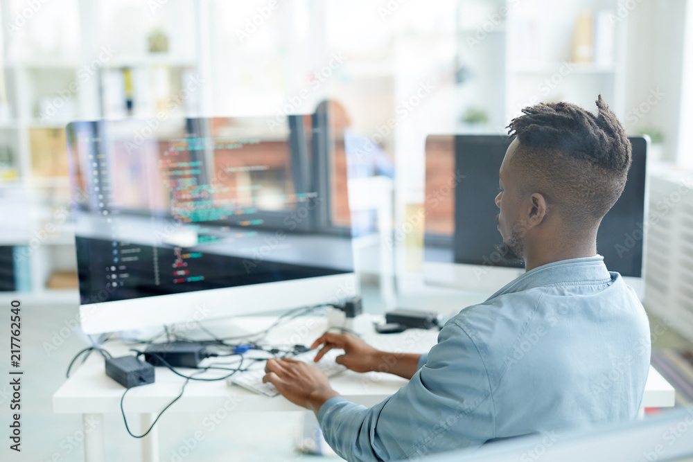Wall mural back view of young african-american specialist testing new software while sitting in fornt of comput