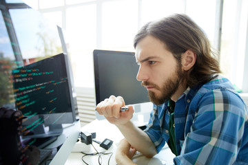 Concentrated young software developer looking at data code on computer screen