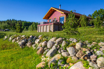 Fototapeta na wymiar Vacation home. House on a sunny day. Cottage in the background of the blue sky. Decorating the territory of the house with a natural stone. Cottage on a hillside.