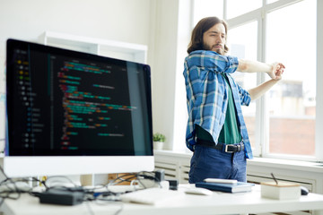 Young programmer stretching his arms while keeping hands together during break for relax in office