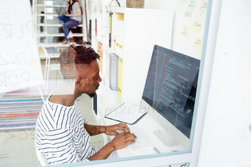 African-american it-specialist looking attentively at coded data on computer screen while working in office