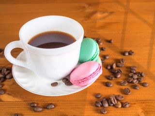 Cup with coffee, cakes and coffee beans on a wooden background lit by the sun with a shadow from the window