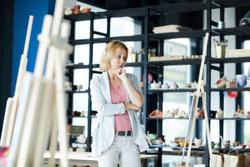 Obraz premium Pensive elegant coach standing by easel and looking at work of one of trainees in studio of artwork