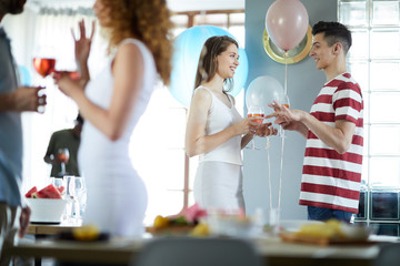 Young couple with drinks having talk at birthday party in festive atmosphere