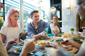 Laughing guy giving pizza to one of his friends by dinner in modern cafe or restaurant
