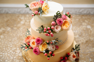 Obraz na płótnie Canvas Photo of wedding cake with gold plating. The three-tiered cake for the wedding is painted with beautiful large live flowers.