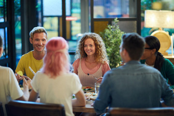 Happy guy and girl looking at their friends by served table during talk in cafe or restaurant