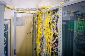 Messy internet wires have a connection to computer servers. Cabinets with computer equipment are...