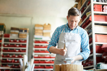 Fototapeta premium Young artisan with handtool hammering marble or stone workpiece in his workshop