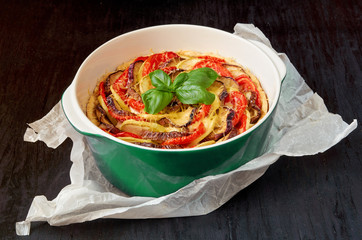 Traditional French dish quiche with eggplants and tomatoes in the green baking dish decorated with fresh basil leaves. Homemade vegetable tart on the black background. Close up view