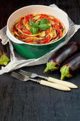 Pie with eggplants and tomatoes in the green baking dish decorated with fresh basil leaves and vintage forks. Homemade vegetable tart on the black background. Side view with copy space for text