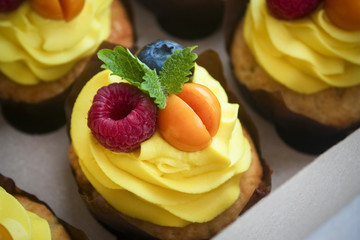 Close up of a vanilla cupcake with yellow Citrus cream, mint, and fresh berries