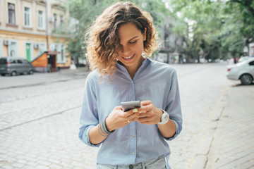 Happy young woman wearing blue shirt using mobile phone
