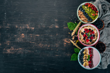 Obraz na płótnie Canvas Oatmeal with yogurt, fruits and berries in plates. Breakfast. On a black wooden background. Top view. Free space for text.