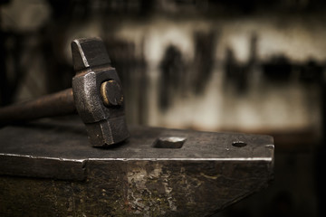 Close-up of heavy hammer placed on durable steel anvil in dark smithery