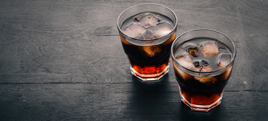Whiskey with ice in a glass. Rum-Cola. Brandy. On a black wooden background. Top view. Free space...