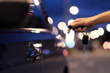 Close-up of a female hand pressing a button on a key ring of car keys, against the background of a car door.
