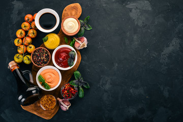 Set of sauces - Ketchup, mayonnaise, mustard, soy sauce, barbecue sauce, pepper and spices. On a black stone background. Top view. Free space for text.