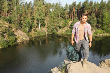 Fototapeta na wymiar Young man on rock near lake and forest. Camping season