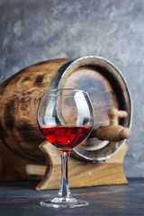 Glass with red wine for tasting and wooden barrel in dark cellar