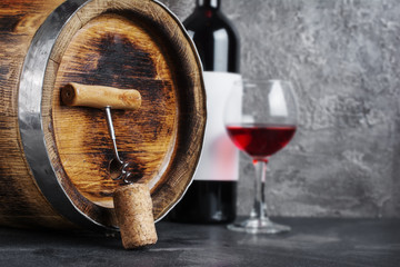 Red wine bottle with glass for tasting and wooden barrel with corkscrew in dark cellar