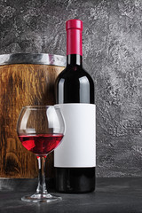 Red wine bottle with glass for tasting and wooden barrel in dark cellar