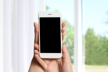 Woman holding smartphone with blank screen on blurred background. Mockup for design