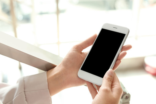 Woman holding smartphone with blank screen on blurred background. Mockup for design