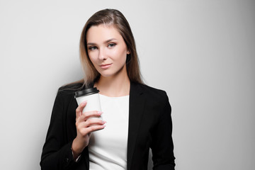 Beautiful businesswoman office worker resting, drinking and holding a paper glass with coffee. White background, Black suit and blouse.