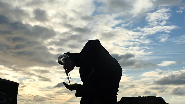 mistic old man in hoodie silhouette with chemical flasks pours a powder