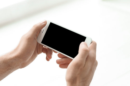 Man holding mobile phone with blank screen on blurred background, closeup. Mockup for design