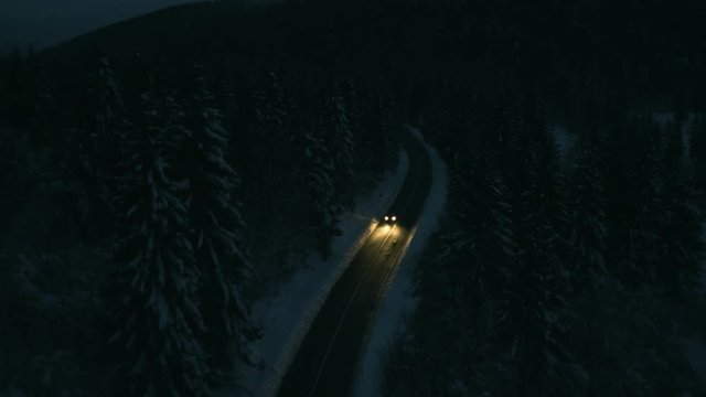Aerial shot of a car driving through an icy spruce forest at night.