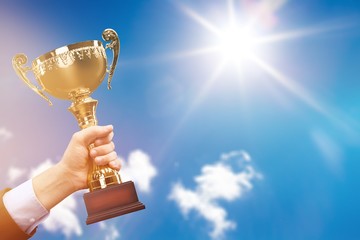 Hand holding golden trophy on sky background