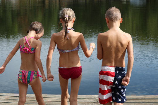 Three wet children in their swimsuit seen from behind on a dock by the water