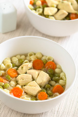 Homemade chicken soup with pea, carrot and small shell pasta in bowls, photographed with natural light (Selective Focus, Focus in the middle of the first soup)