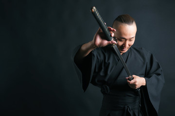 A samurai man in black kimano pulls out his sword on a black background