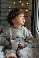 Little boy waiting for Santa Clause. Cute curly toddler boy sitting near the window