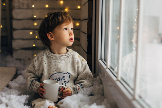 Little boy waiting for Santa Clause. Cute curly toddler boy sitting near the window