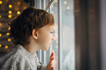 Little boy waiting for Santa Clause. Cute curly toddler boy sitting near the window