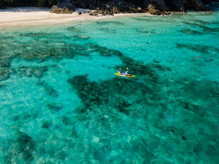 Aerial drone view of a sea kayak exploring a beautiful tropical coral reef next to a remote island
