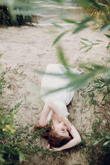 beautiful boho girl lying on sandy beach at sunset light near lake. attractive young woman in white...