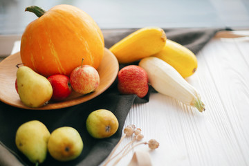 Pumpkin and zucchini in stylish wooden plate with apples and pears on linen apron on white wooden table in light.  Hello autumn concept and Fall Harvest. Happy Thanksgiving
