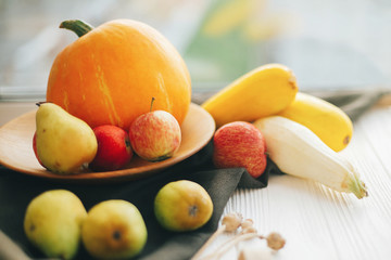 Pumpkin and zucchini in stylish wooden plate with apples and pears on linen apron on white wooden table in light.  Hello autumn concept and Fall Harvest. Happy Thanksgiving